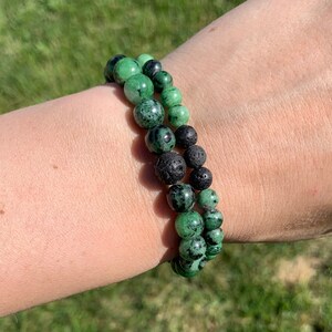 May include: Two bracelets, one with green and black beads and one with black lava rock beads.