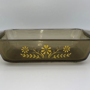 May include: A brown glass loaf pan with yellow floral design. The pan has two handles on the sides.
