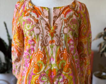 May include: A long-sleeved tunic with a colorful paisley pattern in shades of orange, pink, yellow, and green. The tunic has a scoop neckline with a small V-shaped opening. The fabric appears to be lightweight.