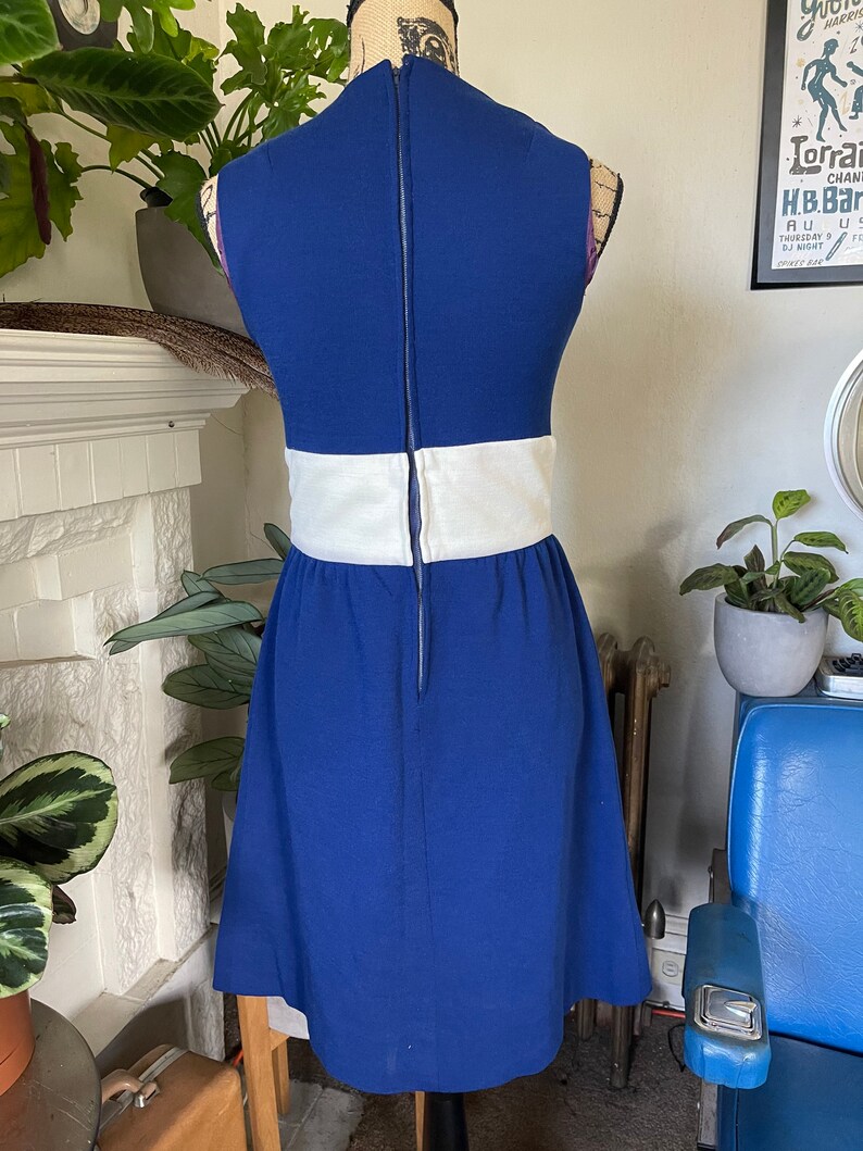 Peut inclure: Une robe bleue sans manches avec une bande blanche autour de la taille. La robe a une fermeture &eacute;clair dans le dos.