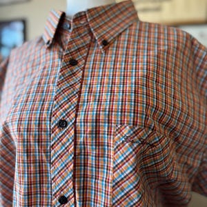 Puede incluir: Camisa abotonada con estampado de cuadros en naranja, azul, rojo y blanco. La camisa tiene cuello abotonado, bolsillo en el pecho y botones negros. El logo de Ben Sherman est&aacute; bordado en el bolsillo.