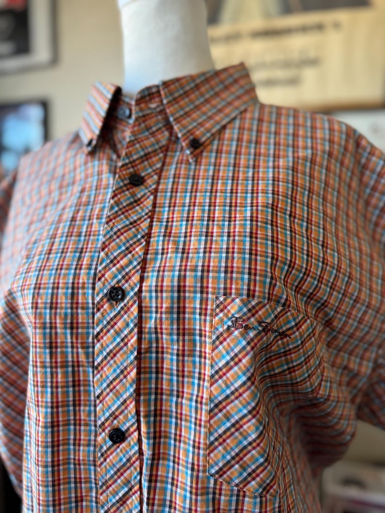 Puede incluir: Camisa abotonada con estampado de cuadros en naranja, azul, rojo y blanco. La camisa tiene cuello abotonado, bolsillo en el pecho y botones negros. El logo de Ben Sherman est&aacute; bordado en el bolsillo.