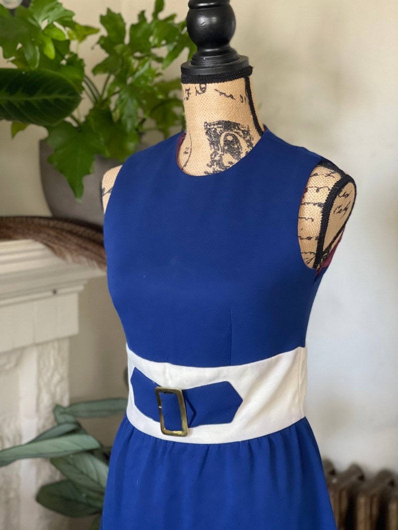 Peut inclure: Une robe bleue sans manches avec une ceinture blanche et une boucle dor&eacute;e. La robe a un design simple et classique.