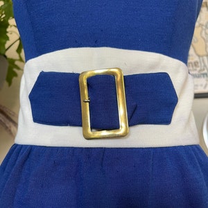 Peut inclure: Une robe sans bretelles bleue et blanche avec une ceinture &agrave; boucle dor&eacute;e.