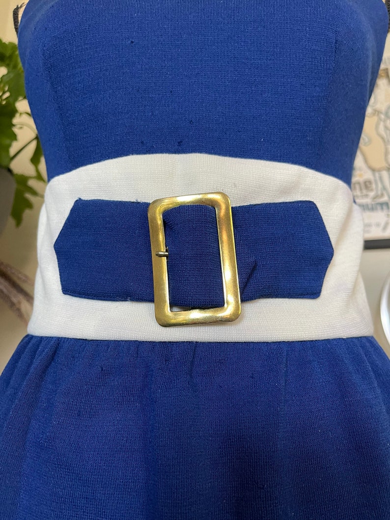 Peut inclure: Une robe sans bretelles bleue et blanche avec une ceinture &agrave; boucle dor&eacute;e.