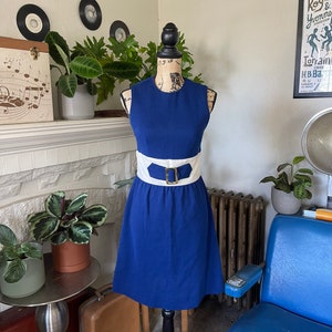 Peut inclure: Une robe sans manches bleu roi avec une ceinture blanche et une boucle dor&eacute;e. La robe a un corsage ajust&eacute; et une jupe &eacute;vas&eacute;e.
