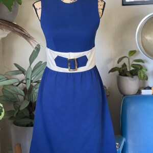 Peut inclure: Une robe bleue sans manches avec une ceinture blanche et une boucle dor&eacute;e. La robe a un corsage ajust&eacute; et une jupe &eacute;vas&eacute;e.
