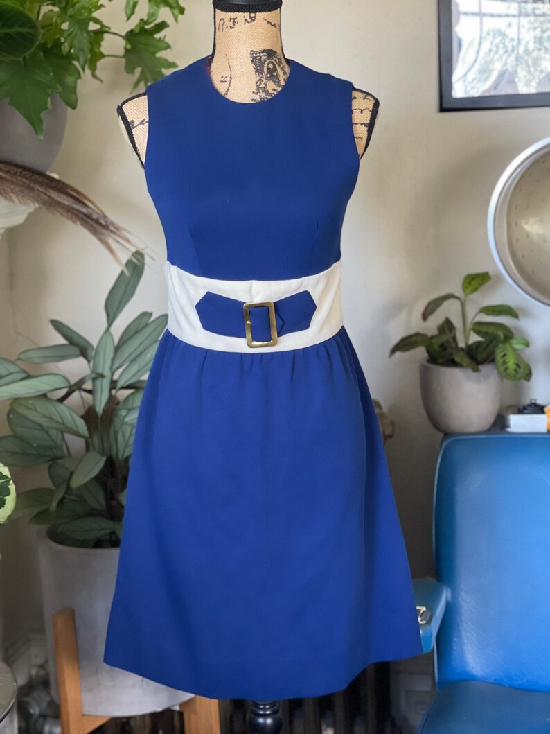 Peut inclure: Une robe bleue sans manches avec une ceinture blanche et une boucle dor&eacute;e. La robe a un corsage ajust&eacute; et une jupe &eacute;vas&eacute;e.