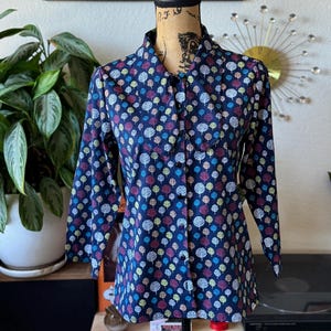 May include: A navy blue long-sleeved button-up shirt with a pattern of colorful trees. The shirt has a collared neckline and a button closure.