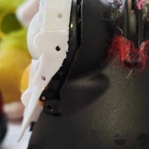 May include: A close-up of a white plastic toy character's head. The character has a black eye and a white plastic piece on the side of its head.