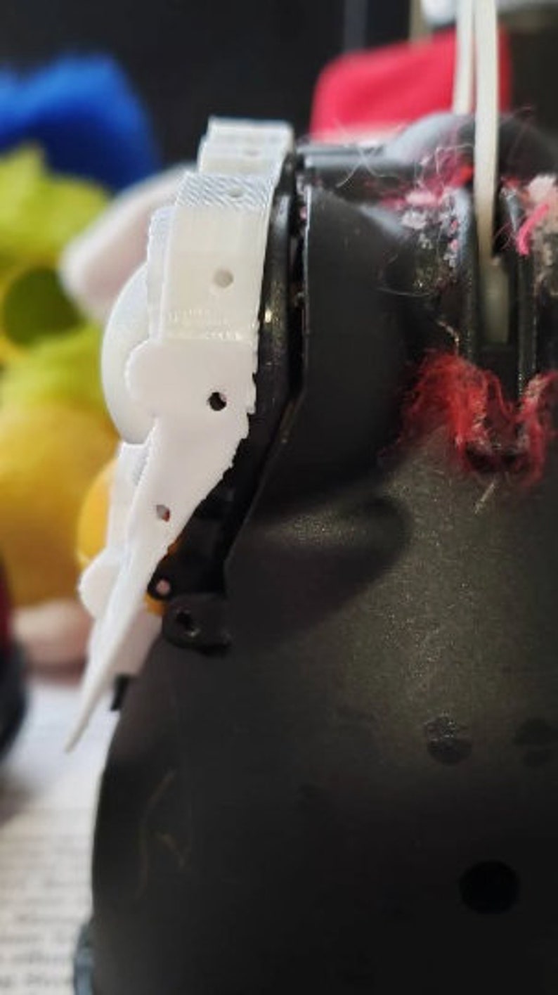 May include: A close-up of a white plastic toy character's head. The character has a black eye and a white plastic piece on the side of its head.