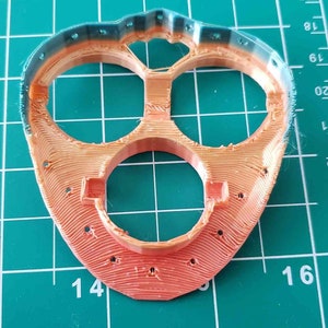 May include: A 3D printed orange and teal plastic part with three circular openings. The part has a textured surface and is designed with a rounded shape.