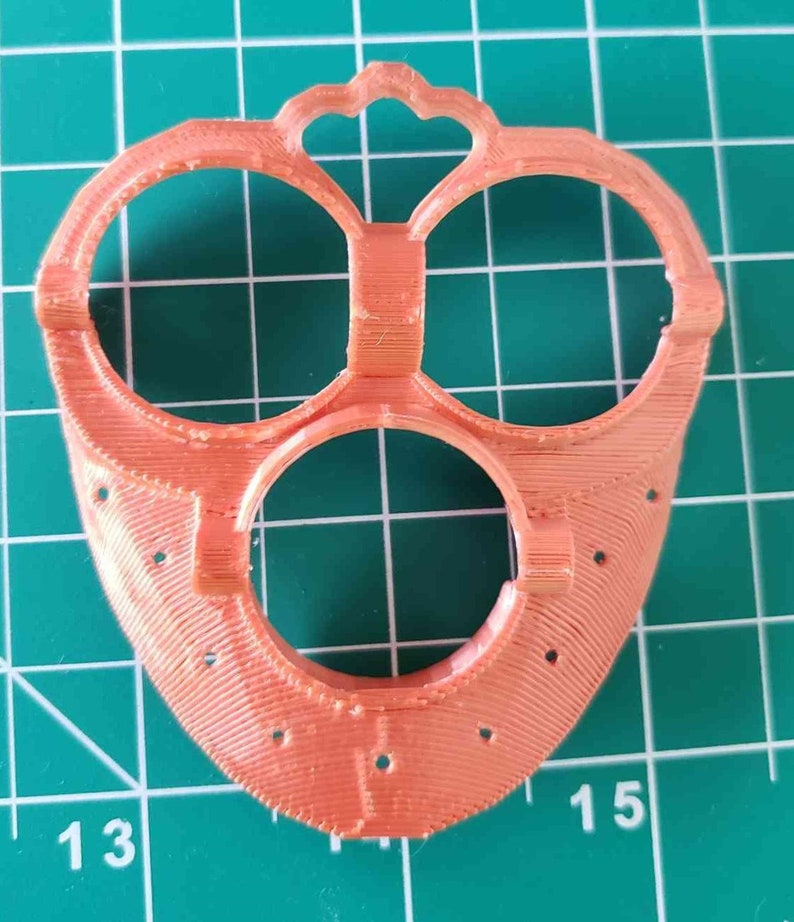 May include: A 3D printed orange plastic part with three circular openings and a decorative design at the top.
