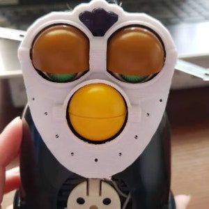 May include: A black and white toy penguin with brown eyes, a yellow beak, and a white face mask. The toy has a round body and a small, round head. The toy is made of plastic and has a hole in the bottom for batteries.