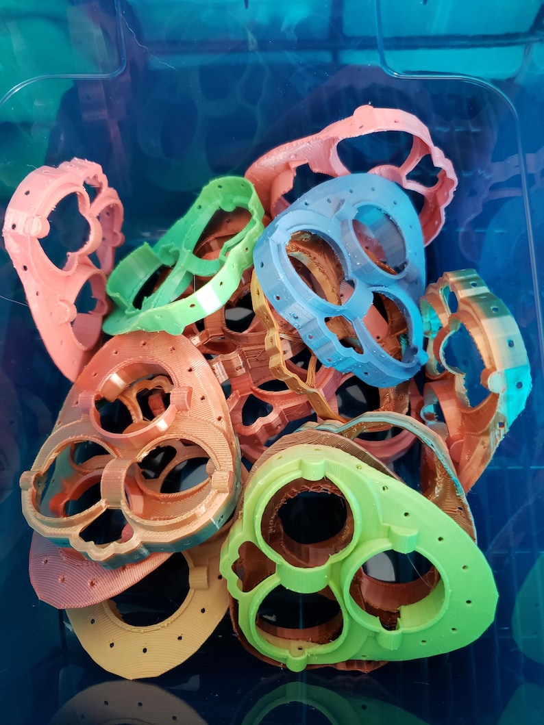 May include: A collection of 3D printed plastic heart-shaped molds in various colors, including green, blue, orange, and pink. The molds have multiple holes and are stacked on top of each other.