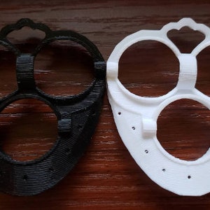 May include: Two 3D printed plastic face masks, one black and one white. Both masks have three circular openings for the eyes and nose.