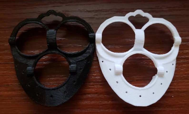 May include: Two 3D printed plastic face masks, one black and one white. Both masks have three circular openings for the eyes and nose.