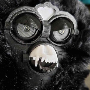 May include: A black furry toy with a white face and large black eyes. The toy has a white mouth with teeth.