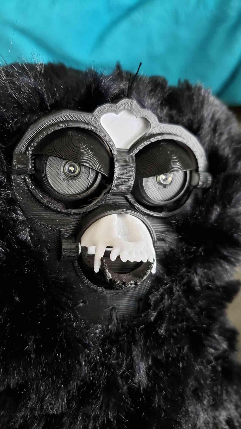 May include: A black furry toy with a white face and large black eyes. The toy has a white mouth with teeth.