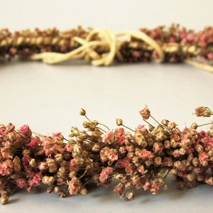 Op de afbeelding: Een krans van gedroogde bloemen gemaakt van kleine roze en bruine bloemen. De krans is geweven met een natuurlijke touw.