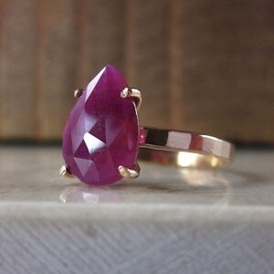 Op de afbeelding: Een ring met een peervormige robijn edelsteen, gezet in een gouden band. De robijn is diep roze van kleur en heeft een facetgeslepen vorm.