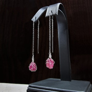 Puede incluir: Un par de pendientes de plata con gotas de piedras preciosas rosas. Las piedras preciosas están envueltas en alambre de plata y cuelgan de delicadas cadenas de plata.