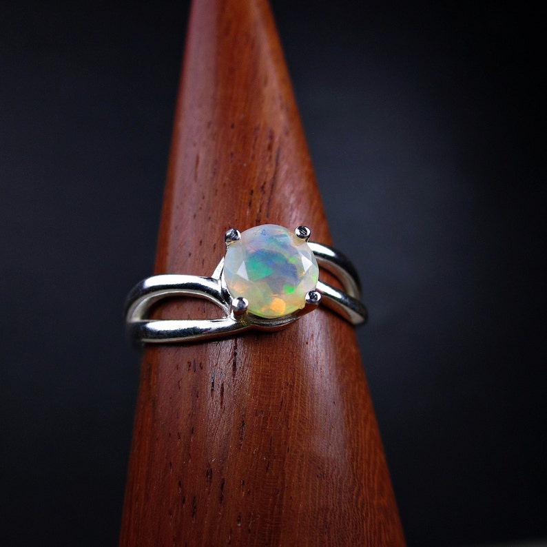 Puede incluir: Un anillo de plata con una piedra preciosa de &oacute;palo blanco engastada en un delicado dise&ntilde;o de doble banda.