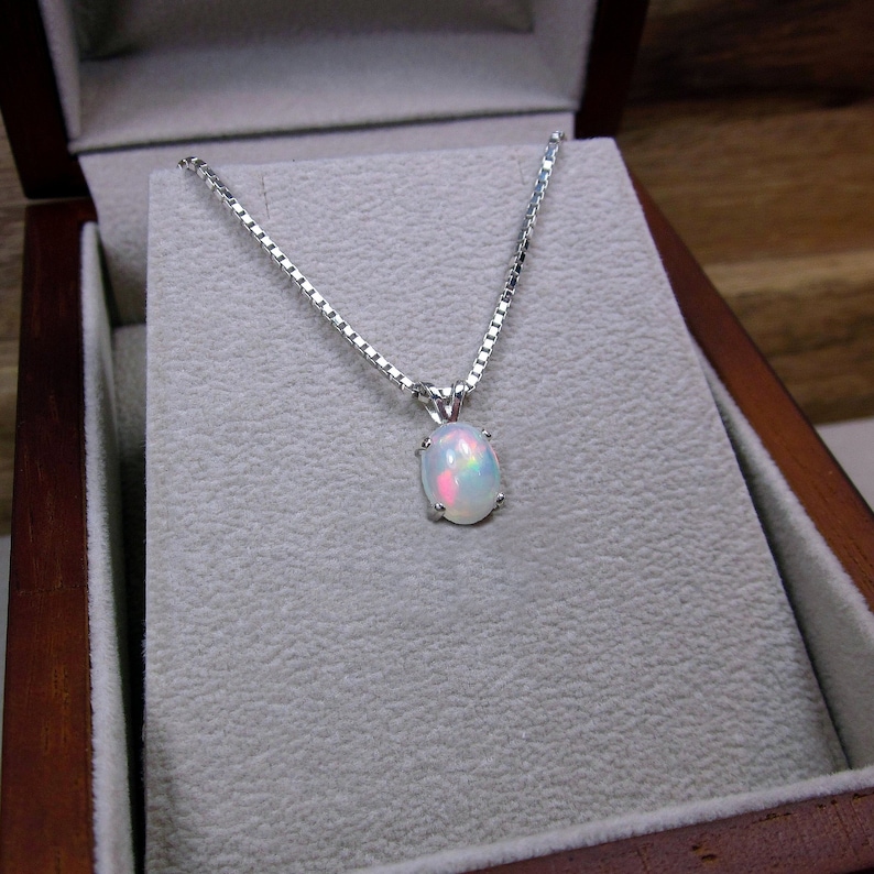 May include: A silver chain necklace with a white opal pendant in an oval shape. The pendant has a rainbow iridescent effect.