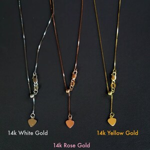 K&ouml;nnte beinhalten: Drei Halsketten aus Wei&szlig;-, Ros&eacute;- und Gelbgold mit Herzanh&auml;ngern. Die Ketten sind vor dunklem Hintergrund abgebildet, mit den Bezeichnungen: 14k White Gold, 14k Rose Gold und 14k Yellow Gold. Die Ketten haben feine Glieder.
