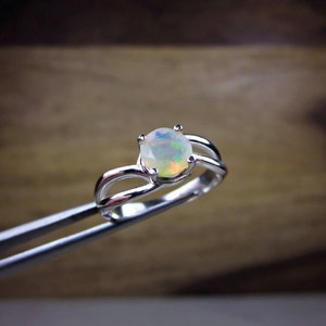 Puede incluir: Un anillo de plata con una piedra de &oacute;palo blanco. El anillo tiene una banda delicada y retorcida.
