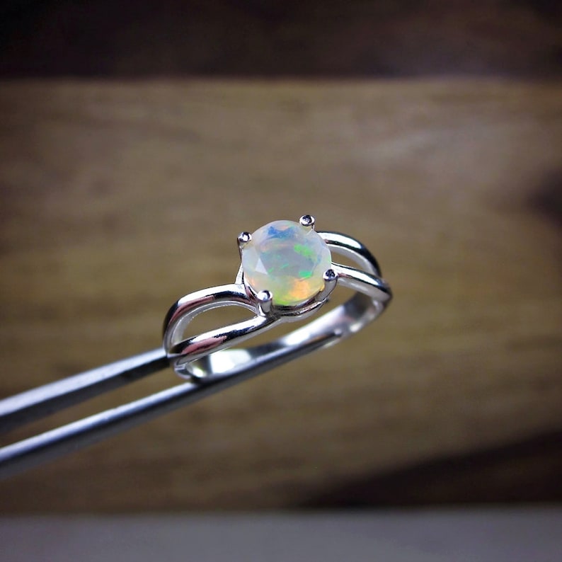 Puede incluir: Un anillo de plata con una piedra de &oacute;palo blanco. El anillo tiene una banda delicada y retorcida.