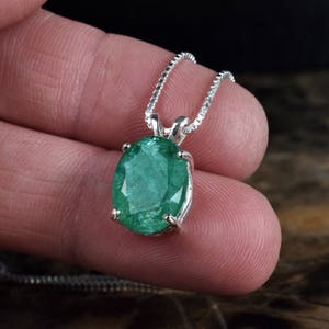 Pode incluir: Um colar de corrente de prata com um pingente de esmeralda oval verde.