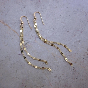 Peut inclure: Une paire de boucles d'oreilles pendantes dorées avec trois brins de chaîne ornés de petits maillons rectangulaires.