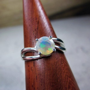 Puede incluir: Un anillo de plata con una piedra de &oacute;palo blanco engastada en una banda delicada y curva.