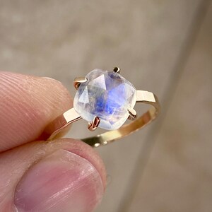K&ouml;nnte beinhalten: Ein goldener Ring mit einem gro&szlig;en, klaren, schillernden Mondstein, der in einer Zargenfassung sitzt. Der Stein hat einen blauen Schimmer.