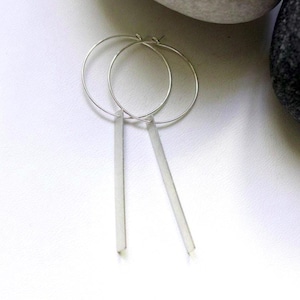 Può includere: Orecchini a cerchio in argento con un pendente lungo e dritto.
