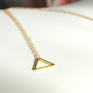 Könnte beinhalten: Eine goldene Kettenkette mit einem einfachen, geometrischen Dreiecksanhänger.