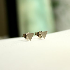 Peut inclure: Une paire de boucles d'oreilles en argent en forme de triangle. Les boucles d'oreilles sont petites et simples, avec une finition brossée.