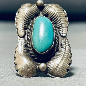 May include: A silver ring with a turquoise stone set in a detailed design. The ring has a textured, ornate design with a central oval-shaped turquoise stone.