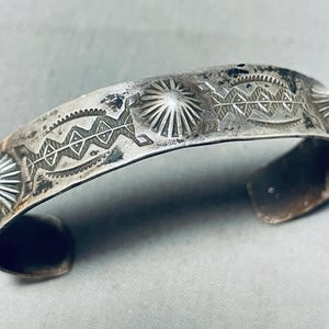 May include: A silver bracelet featuring a geometric design. The bracelet is crafted from a thick band of silver and has a simple, elegant design.