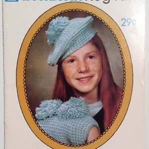 Op de afbeelding: Een vintage Woolworth Rug Yarn-boekje met een jong meisje dat een lichtblauwe gehaakte muts en bijpassende trui draagt. De omslag van het boekje bevat de tekst "Woolworth Rug Yarn" en "29¢".