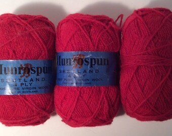 May include: Three balls of red yarn with blue and white labels that read "Munrospun Shetland 4 Ply 100% Pure Virgin Wool Made in Scotland".