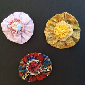 May include: Three fabric flowers, one pink with white polka dots, one yellow with a floral pattern, and one red with a floral pattern.