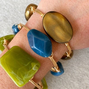 May include: Three gold wire wrapped bracelets with different colored resin beads. The beads are green, blue, and brown.