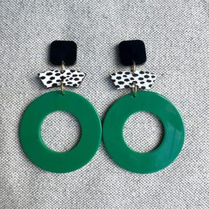 May include: A pair of green circle earrings with black and white patterned accents. The earrings have a black square at the top and a white and black patterned circle in the middle.