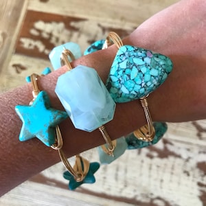 Puede incluir: Cuatro pulseras de alambre dorado con piedras turquesa y blancas. Las pulseras presentan una estrella, una forma geom&eacute;trica y una piedra de forma libre.