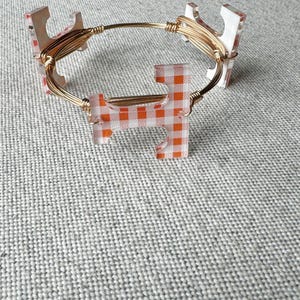 Op de afbeelding: Een gouden draad armband met oranje en witte geruite acryl bedels.