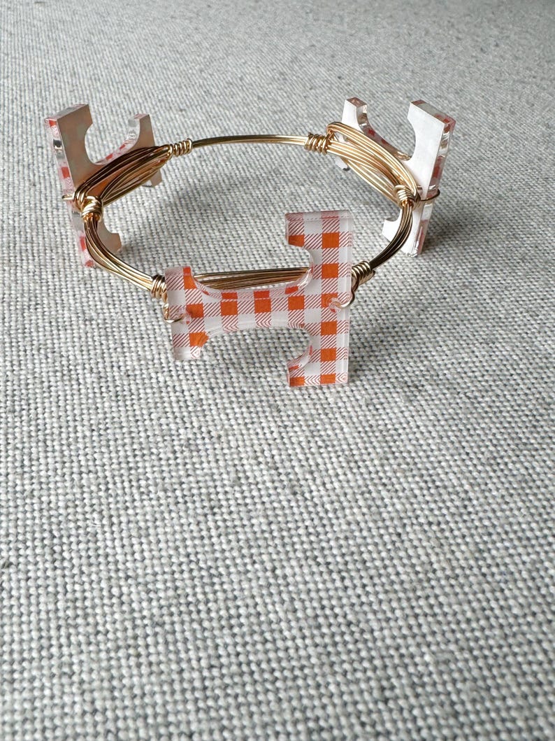Op de afbeelding: Een gouden draad armband met oranje en witte geruite acryl bedels.