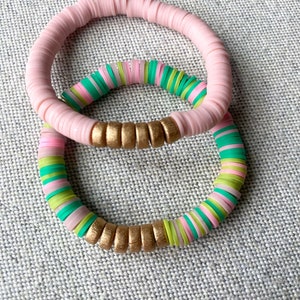 Peut inclure: Deux bracelets, l'un rose et l'autre avec des perles vertes, roses et dorées.