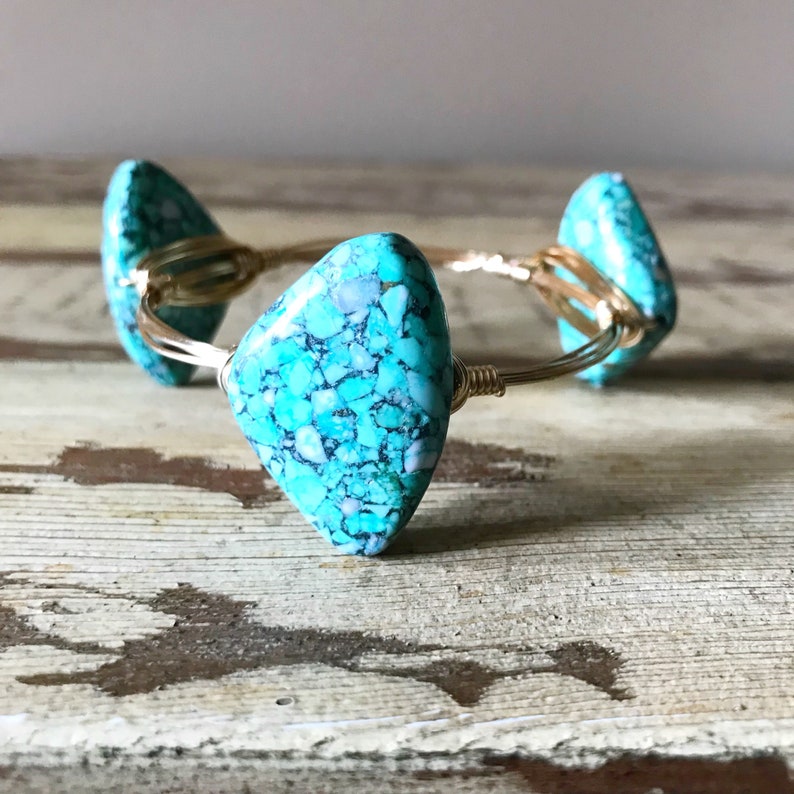 Puede incluir: Un brazalete de alambre dorado envuelto con tres piedras turquesa. Las piedras son de color azul y verde moteado.